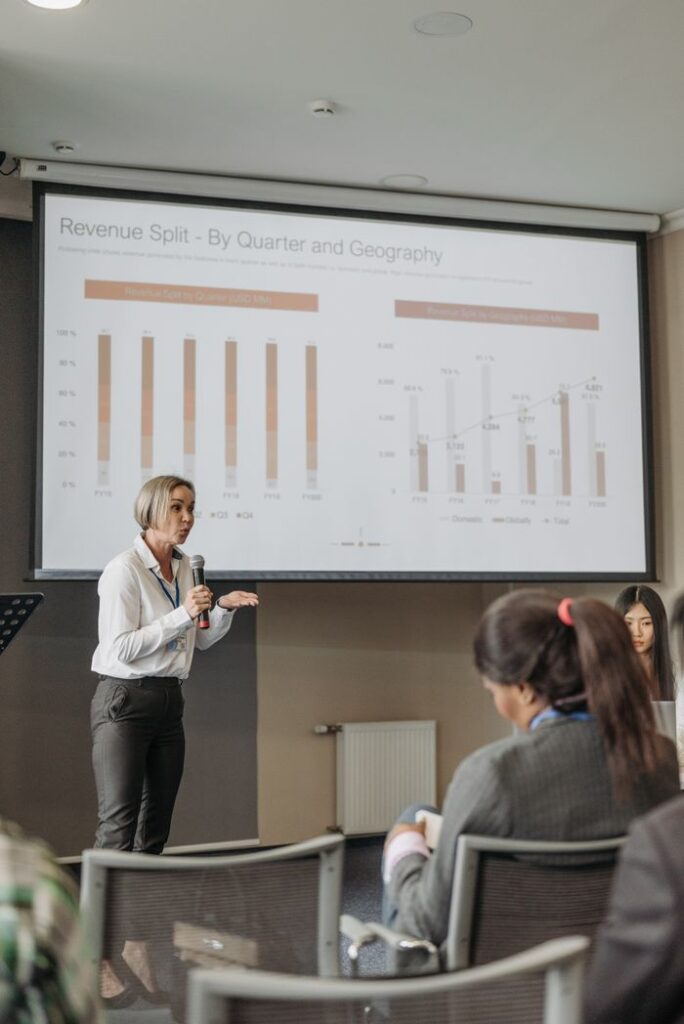 A professional woman leads a seminar on revenue analysis, engaging participants with graphs and data.